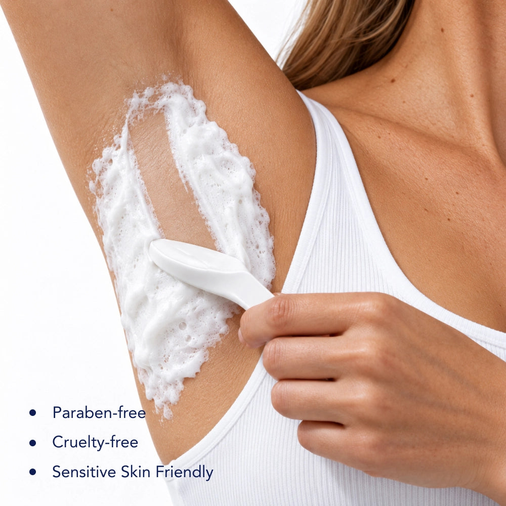 A close-up of a person applying white foaming body wash or shaving lather with a white handheld applicator on their underarm, wearing a white ribbed tank top. Bullet points on the lower left read: 'Paraben-free', 'Cruelty-free', 'Sensitive Skin Friendly'.