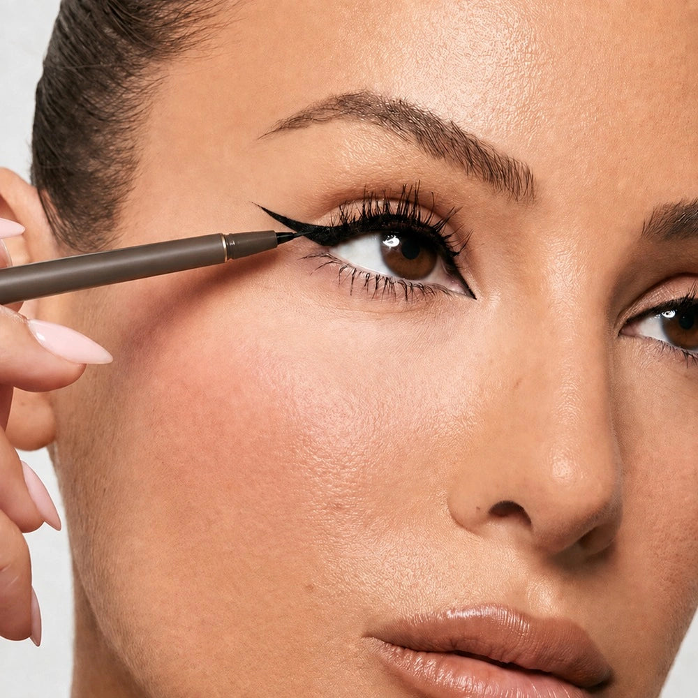 Close-up of a woman applying black liquid eyeliner with a fine brush to her upper lash line.